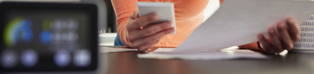 Woman sitting in kitchen using phone and paying bills